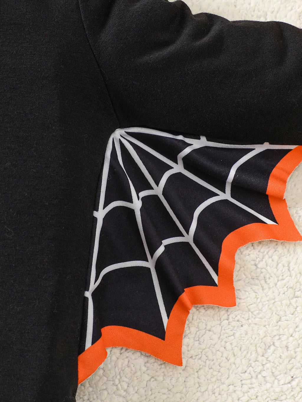 Close-up of a black spiderweb bat wing edged in orange on the Halloween top.