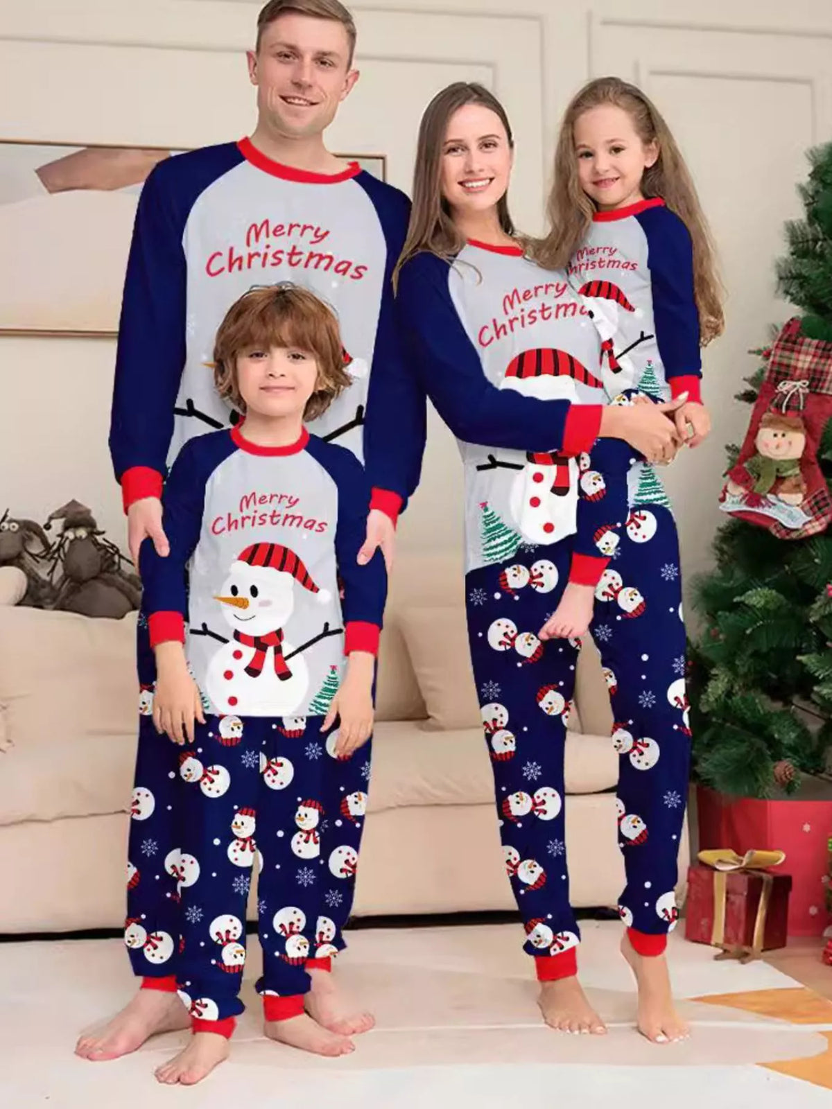 Family wearing white Merry Christmas snowman tops with navy sleeves and navy printed pajama pants.