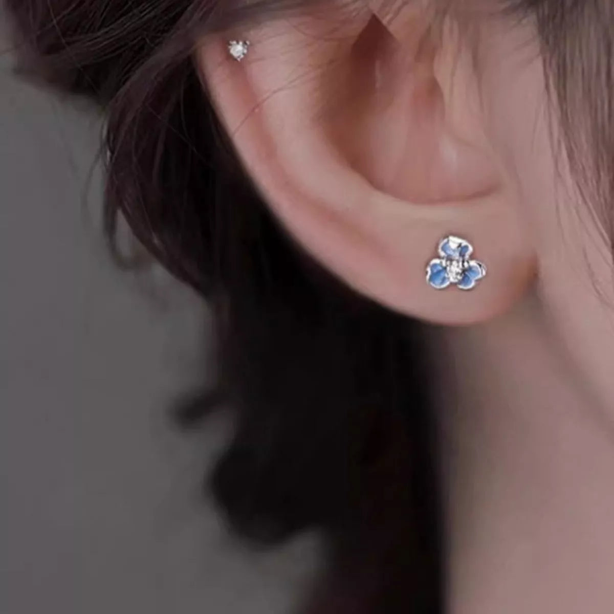 Silver-tone flower stud earrings with blue stones worn on a model
