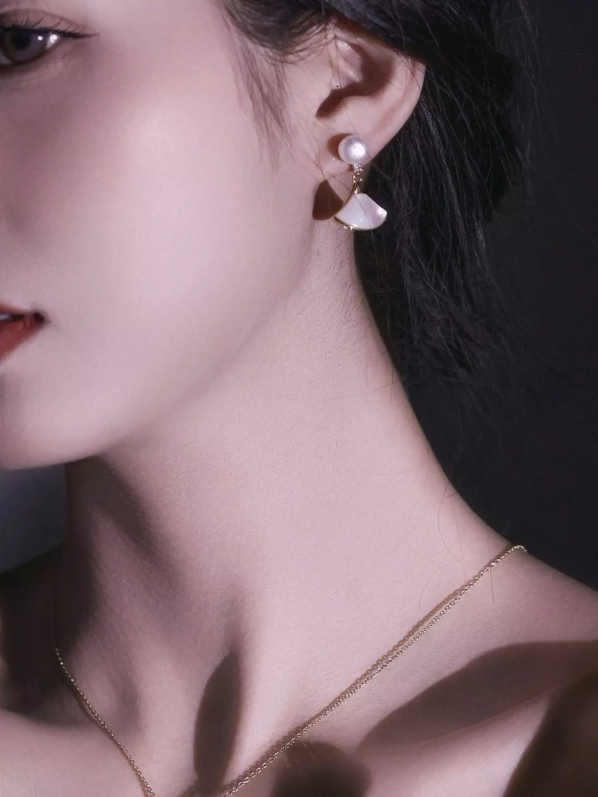 Fan-shaped drop earrings with pearl-like beads and gold-tone edges worn on a model