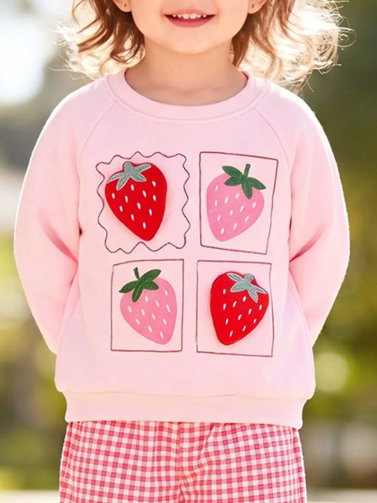 Close view of four strawberry graphics on the child's pink sweatshirt.