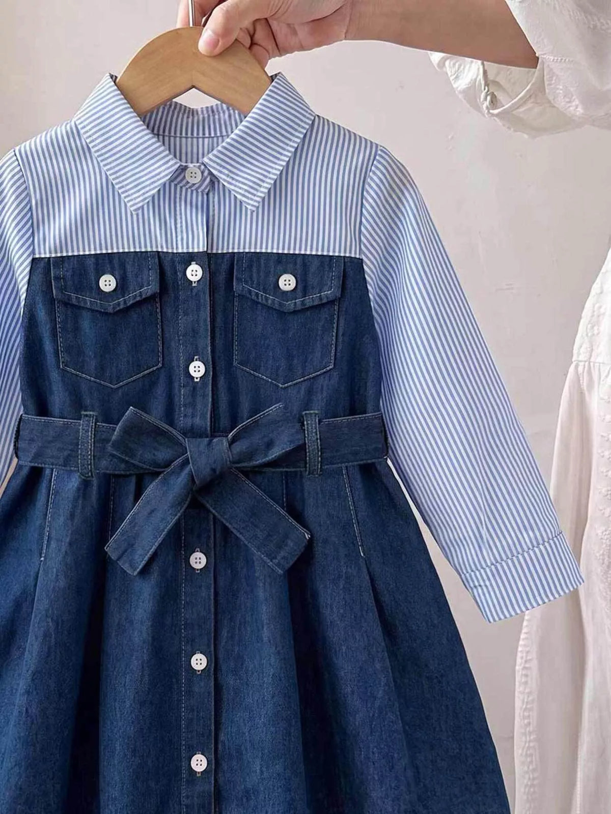 Close view of the striped upper panel and dark blue button-front dress with waist bow.