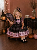 Child wearing a black lace Halloween dress with pink pumpkin border and matching bow headband.