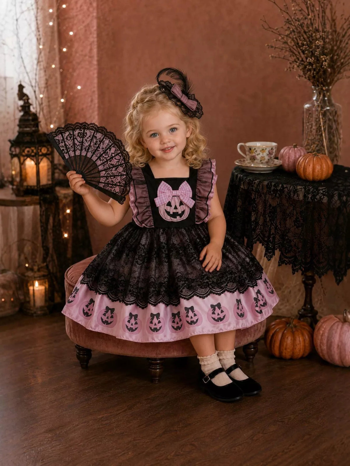 Child wearing a black lace Halloween dress with pink pumpkin border and matching bow headband.