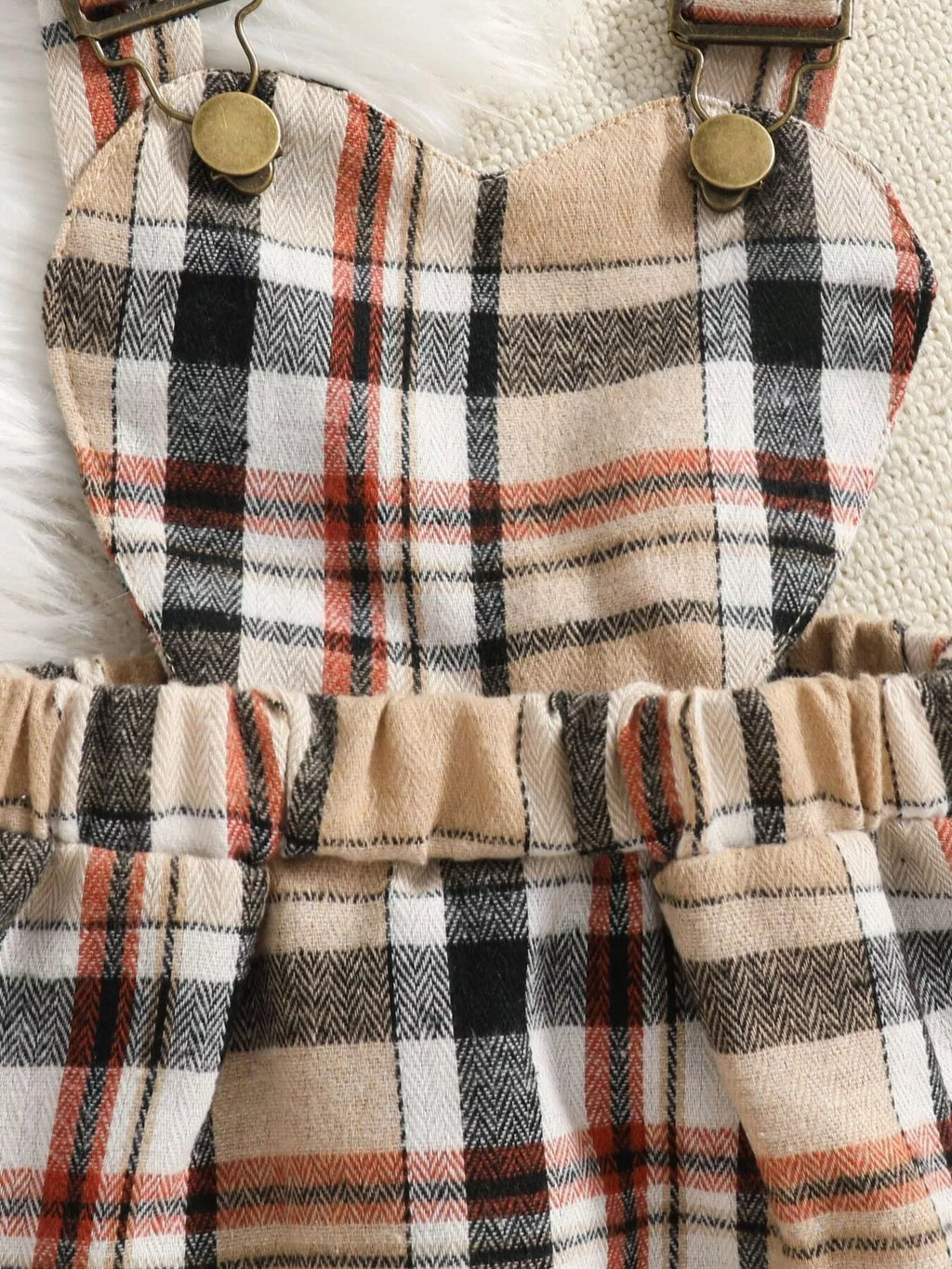 Close-up of the beige plaid skirt's straps, buttons and gathered waistband.