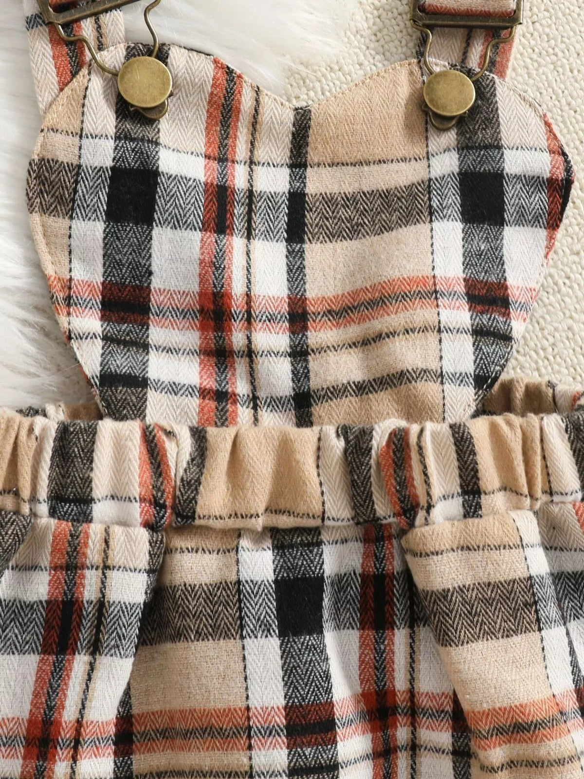 Close-up of the beige plaid skirt's straps, buttons and gathered waistband.